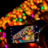 キャンドルナイトをスマホで撮影する手元と暖色の夜景の写真