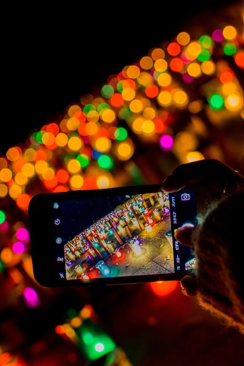 キャンドルナイトをスマホで撮影する手元と暖色の夜景