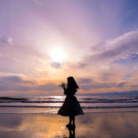 海辺の砂浜で夕日に向かって立つ人のサンセットの写真