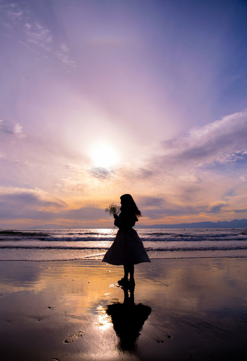 夕暮れの海辺で夕日に向かって立つ人のシルエット