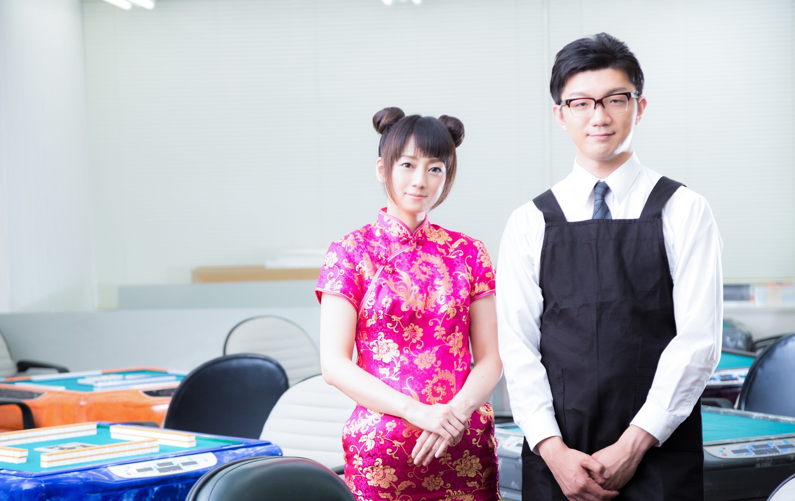 チャイナドレスの女性店員と制服姿の男性が雀荘に立つ［モデル：米崎奈棋 OZPA］