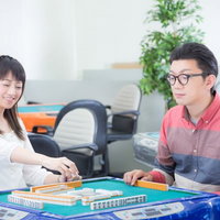 楽しそうに麻雀を打つ男女の対局、テーブルに並ぶ牌と点棒の写真