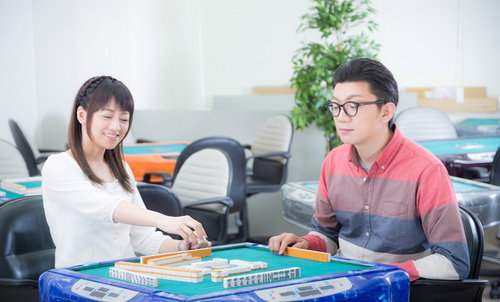 楽しそうに麻雀を打つ男女の対局、テーブルに並ぶ牌と点棒