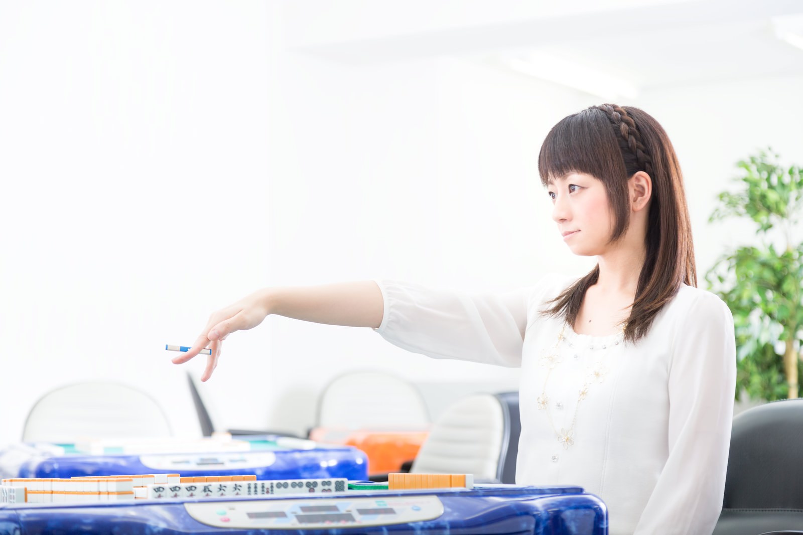 麻雀卓で打牌する白いシャツの女性が横向きで集中している様子［モデル：米崎奈棋］