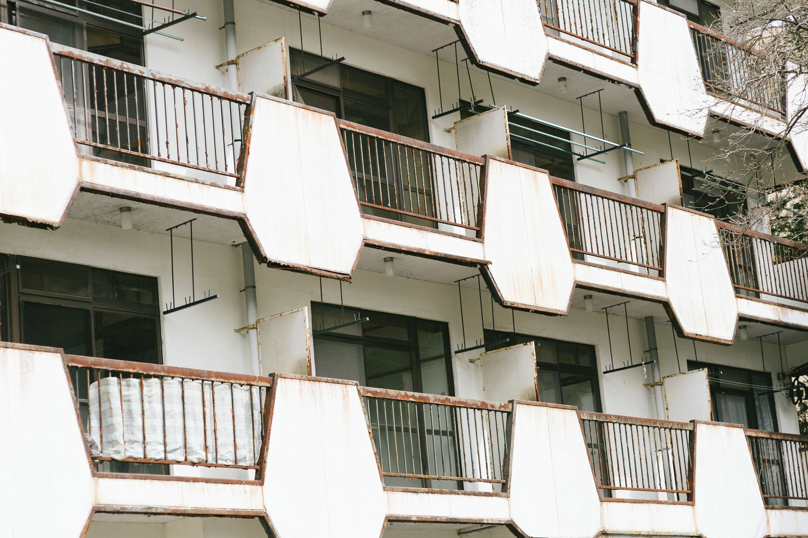 錆びた手すりのバルコニーが並ぶ無人のマンション外観