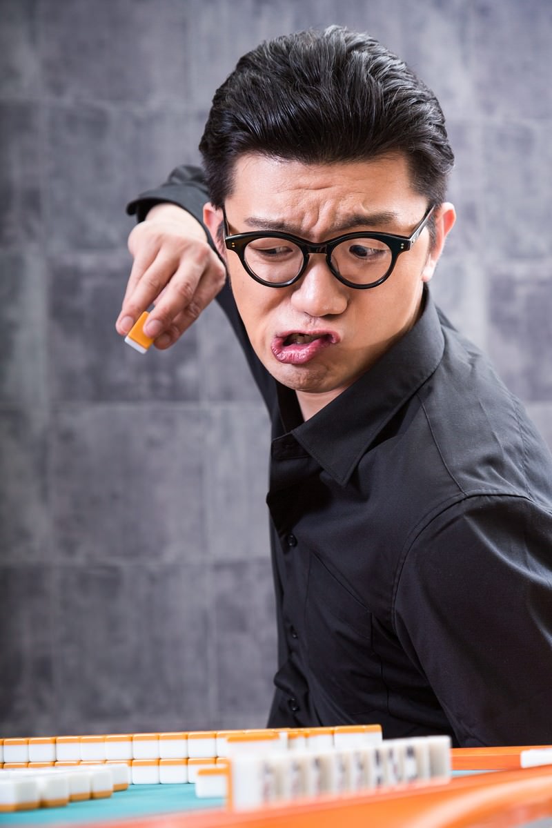 麻雀卓で過剰な仕草でツモを引く眼鏡をかけた男性［モデル：OZPA］