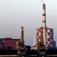 夕方の水辺に並ぶ掘削機と川崎の沿岸の工場の写真