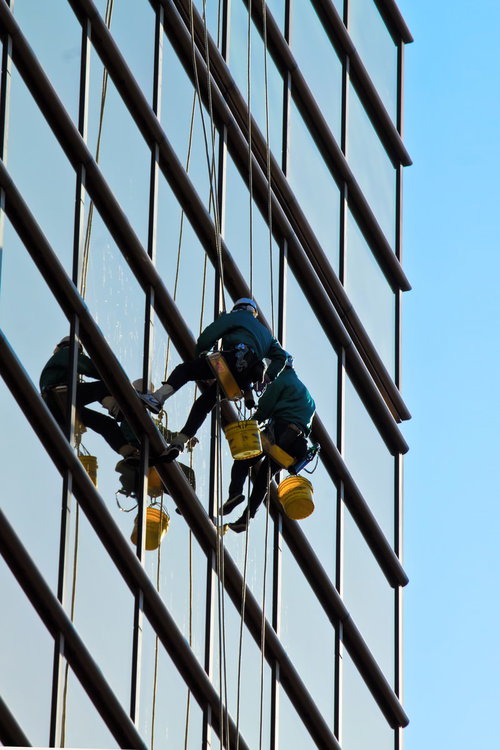 ロープで体を支えてビルの外壁を清掃する高所の窓拭き作業員