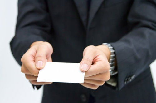 白い名刺を両手で差し出すスーツ姿のビジネスマン