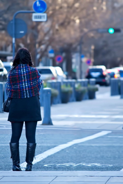 歩道で後ろ姿を見せて信号待ちをする女性