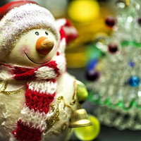 クリスマスツリーの前に置かれた赤い帽子の雪だるま人形の写真