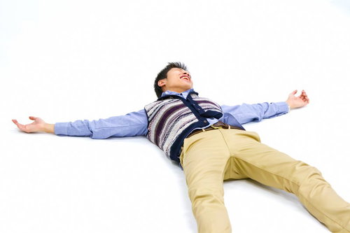 白い背景の上で仰向けに寝て両手を広げる男性