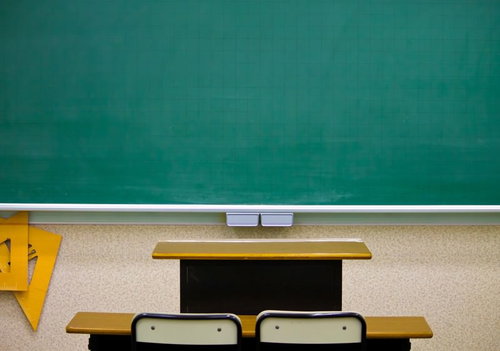 緑の黒板の前に机と椅子が並ぶ教室
