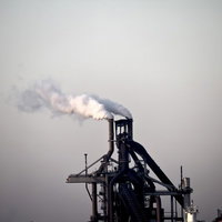 曇り空の下で煙を吐く工場の煙突と設備の写真