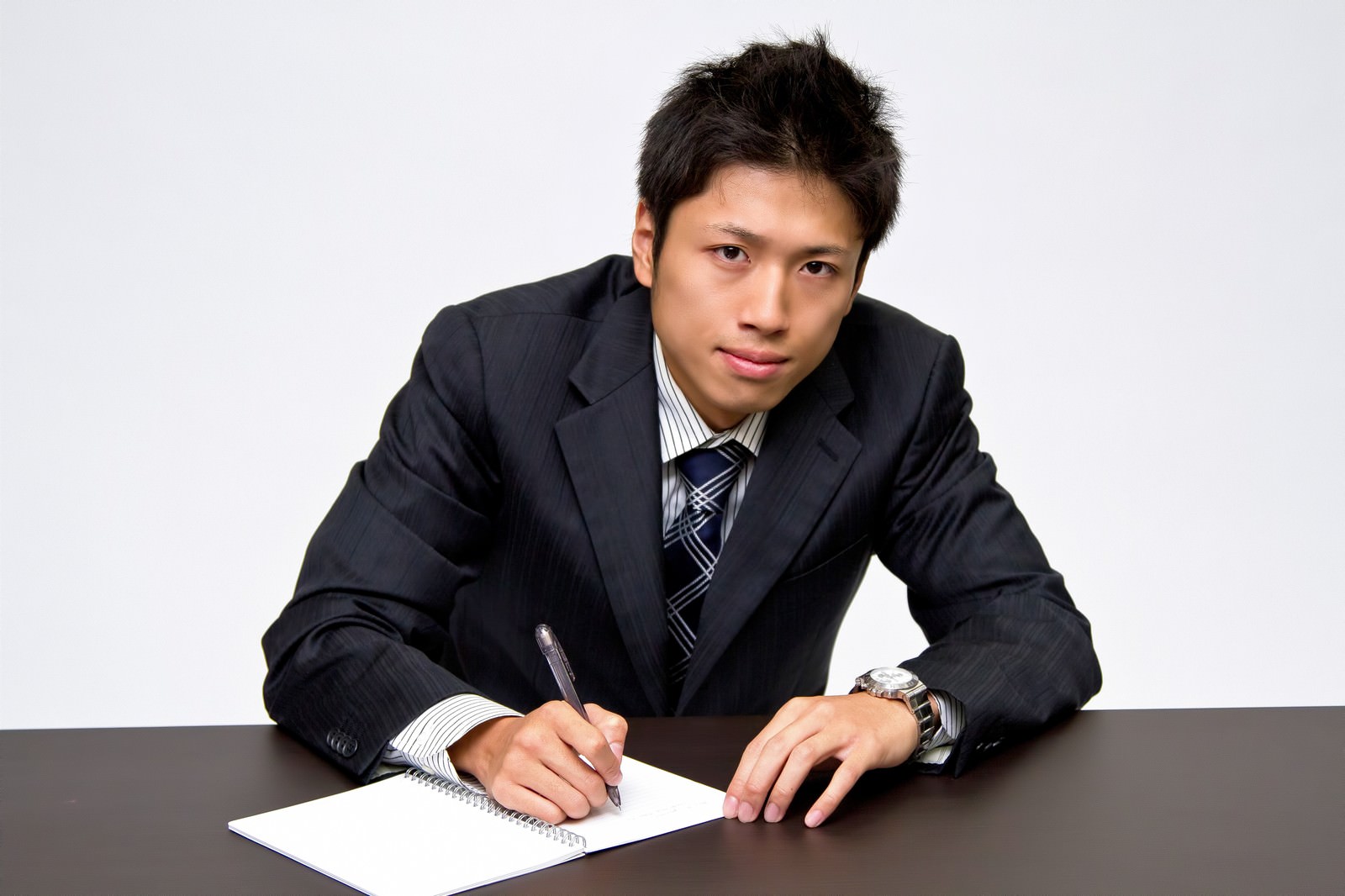 デスクでメモを取るスーツの男性［モデル：恭平］