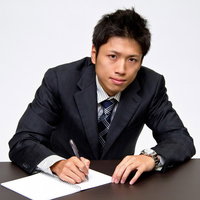 机に向かってメモを取るスーツ姿のビジネスマンの写真