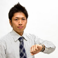 腕時計を確認するネクタイ姿のビジネスマンの写真