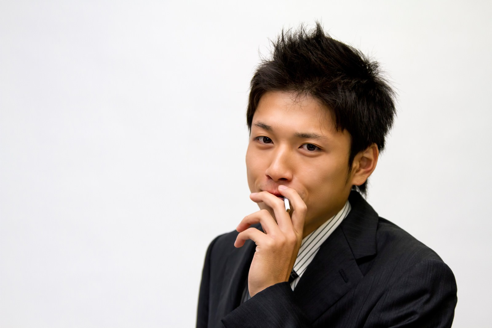 タバコを口元にくわえて正面を見るスーツ姿の若い男性［モデル：恭平］