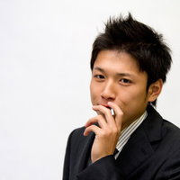 手を口元に当てて座る煙草を吸うビジネスマンの写真