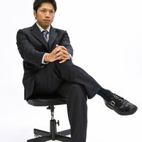 黒い椅子で足を組んで座るスーツ姿のサラリーマンの写真