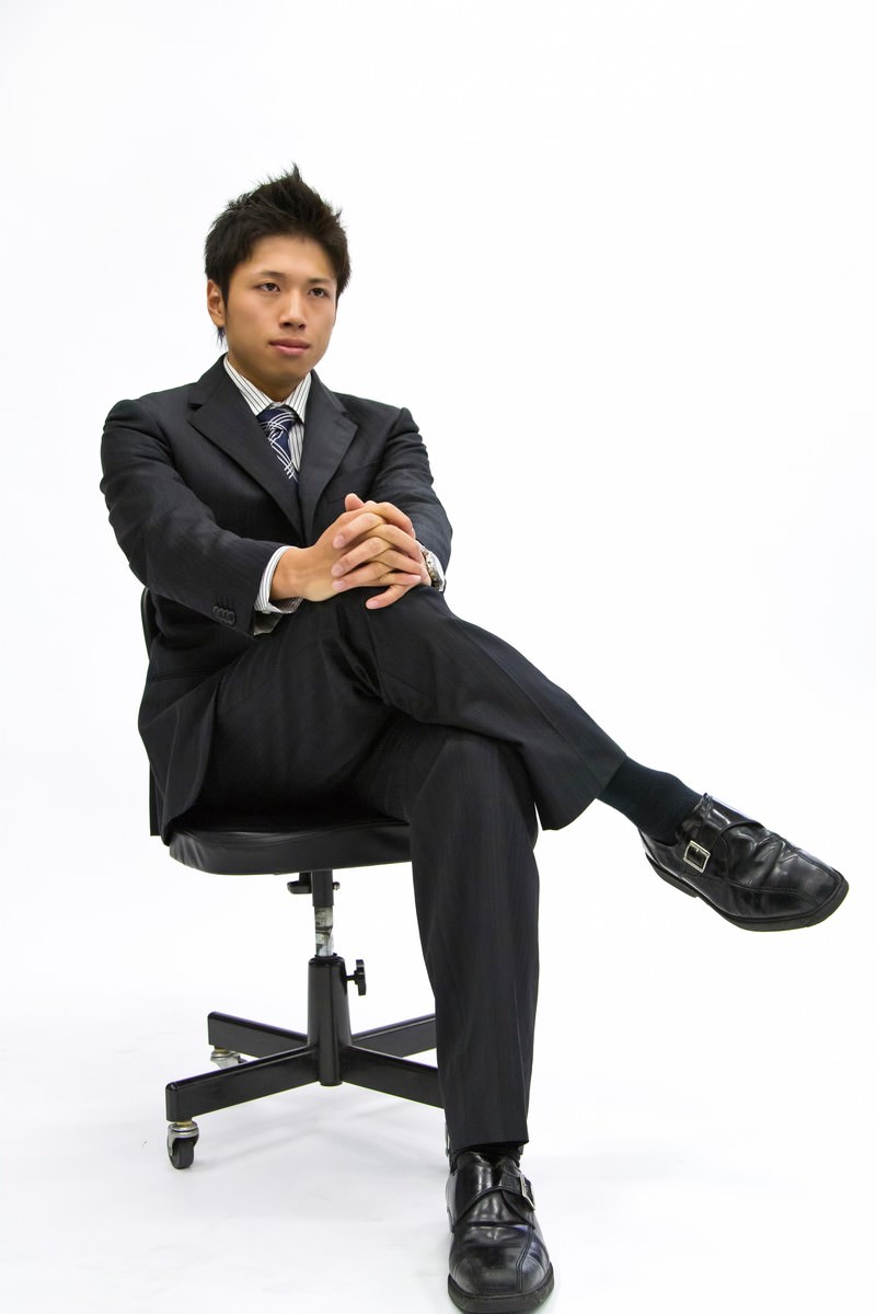 足を組んで椅子に座るスーツの男性［モデル：恭平］