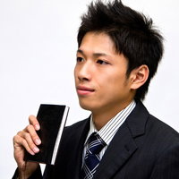 黒い手帳を胸の前に持つスーツ姿のサラリーマンの写真