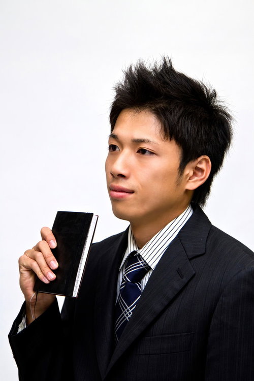 黒い手帳を胸の前に持つスーツ姿のサラリーマン