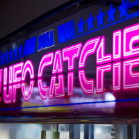 ピンクのネオンが光る古いゲームセンターのUFOキャッチャー看板の写真