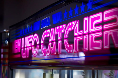 ピンクのネオンが光る古いゲームセンターのUFOキャッチャー看板