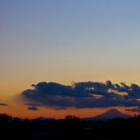 夕焼けの雲の向こうに浮かぶ富士山のシルエットの写真