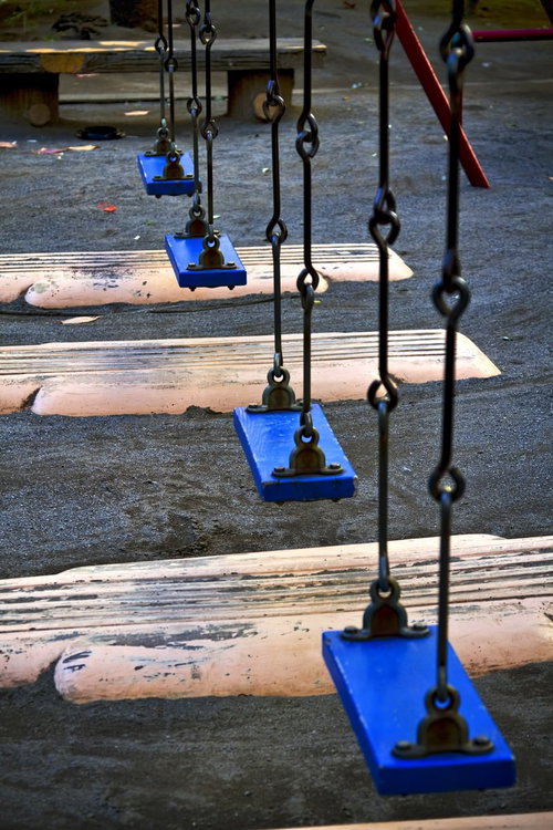 誰もいない公園に並ぶ青いブランコ