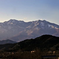 夕方の空に浮かぶ雪が残る山々と住宅地の写真