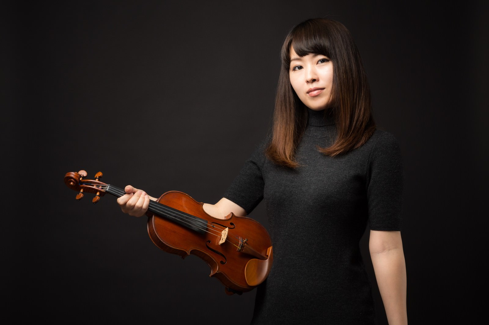 黒い背景の前でヴァイオリンを片手に持ち正面を見つめる女性［モデル：yukiko］