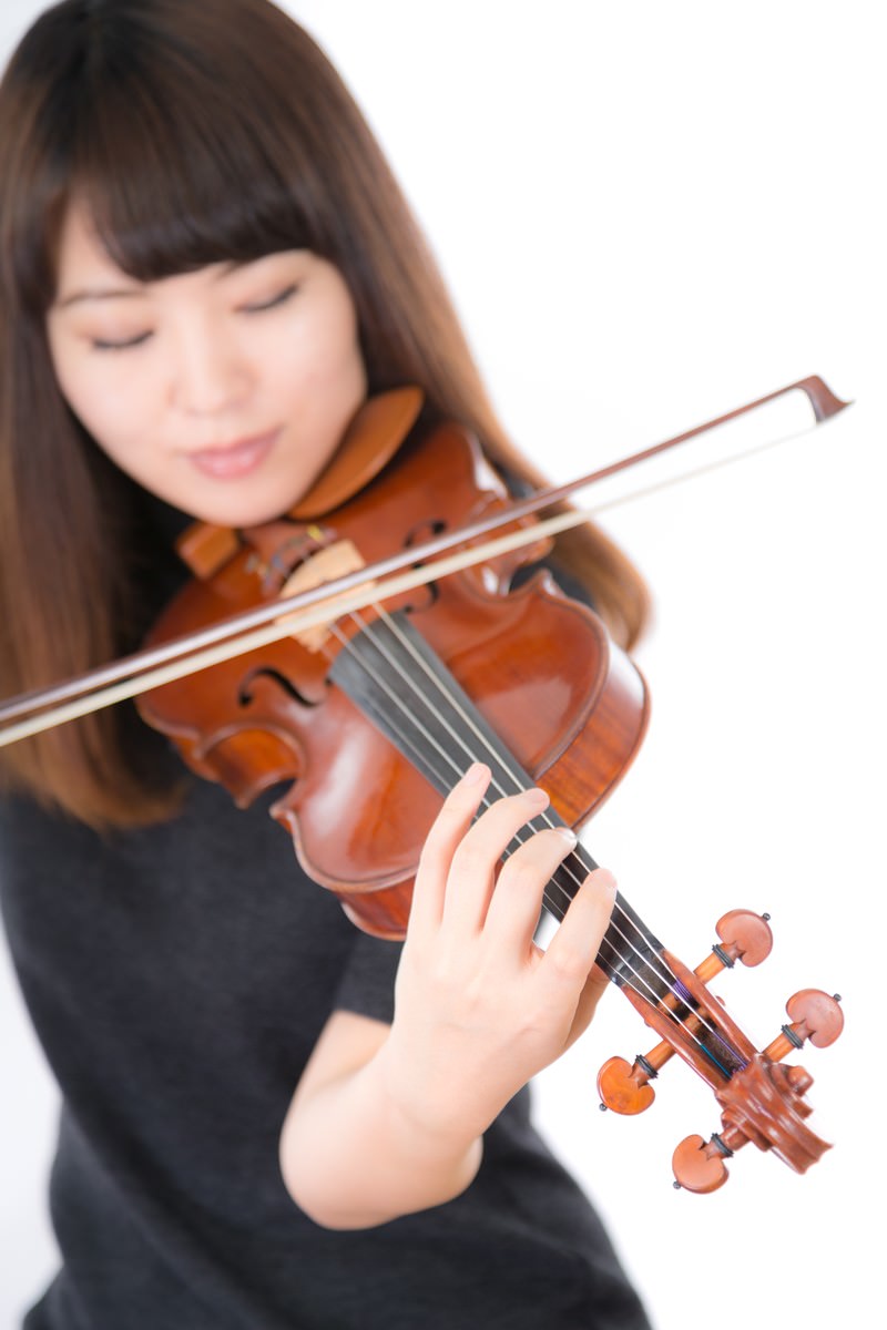 ヴァイオリンを演奏する女性が光の中で楽器を構えている［モデル：yukiko］