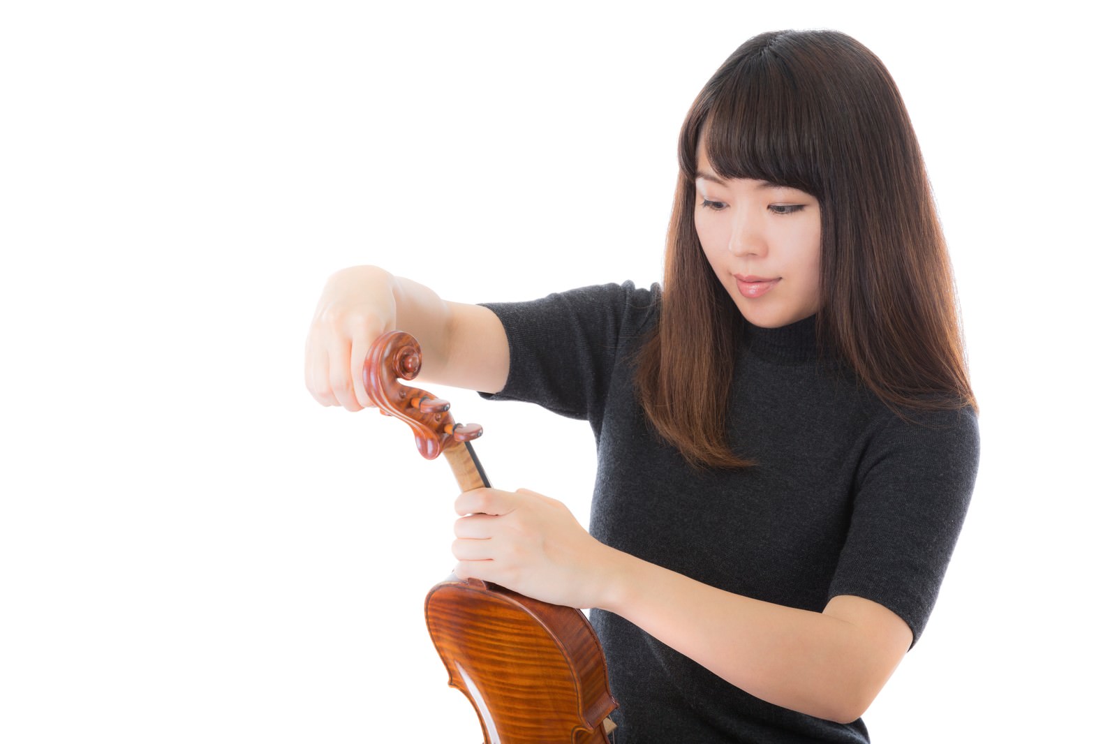 黒いニットを着た女性がヴァイオリンの弦を調整している［モデル：yukiko］