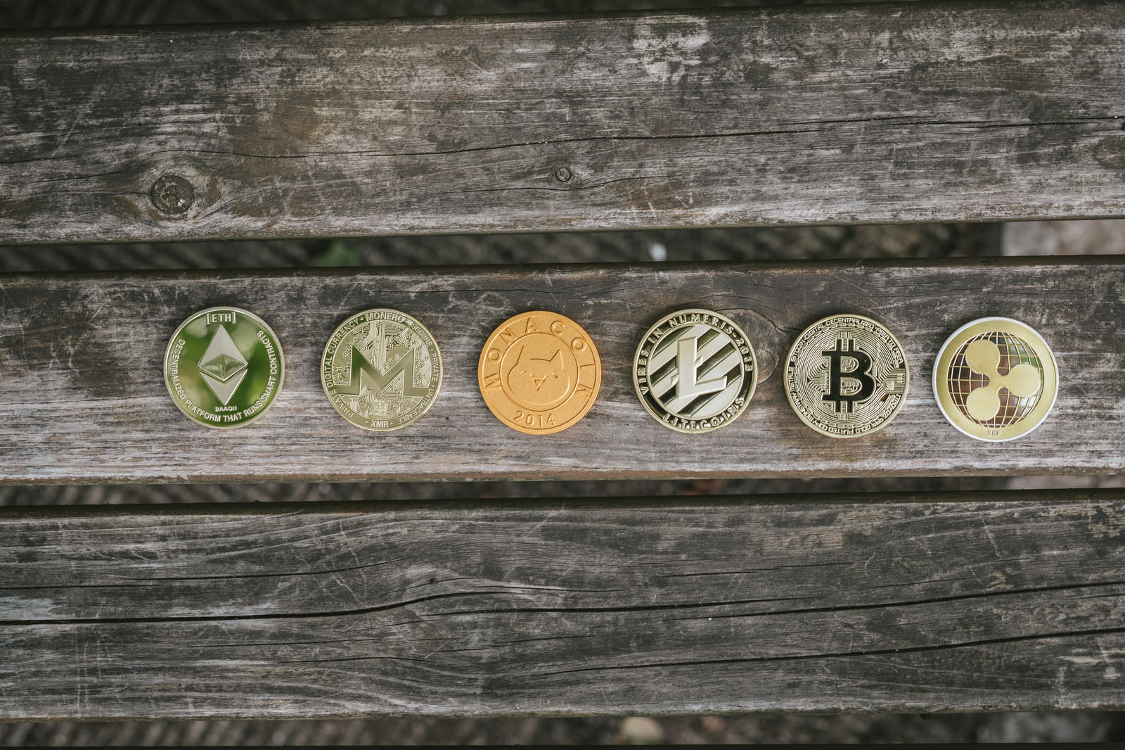 経年劣化した木製テーブルの上に左から6種類の仮想通貨コインが一列に置かれている