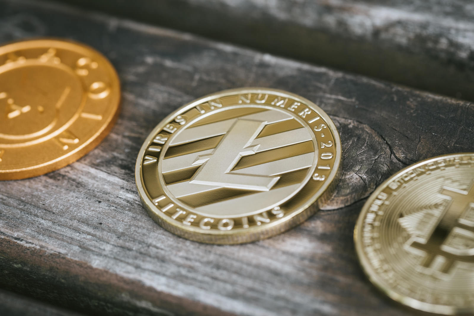 暗号通貨コイン3枚がグレーの木製テーブルに配置され、中央のLTCが銀白色で輝く