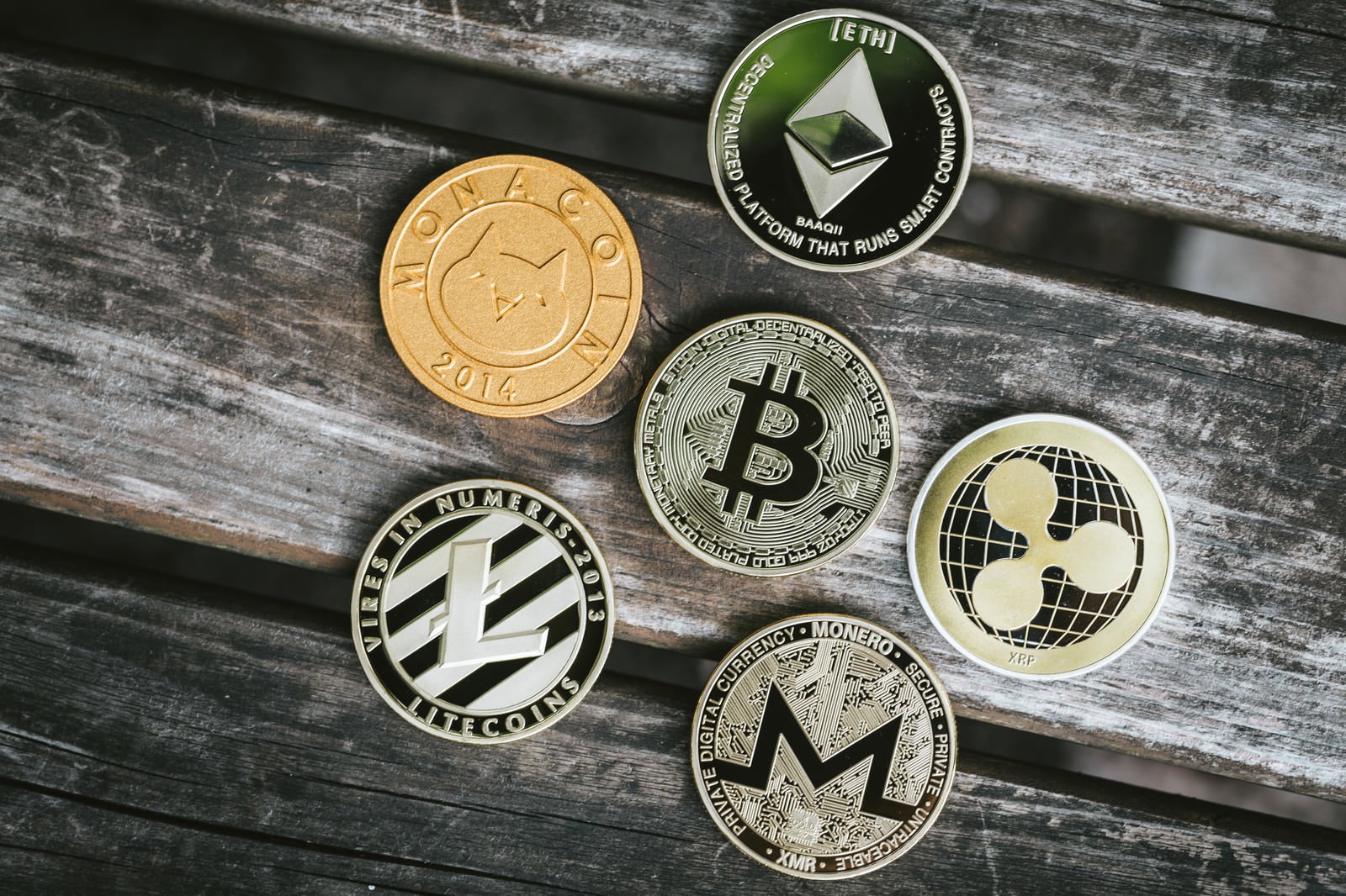 木製テーブル上に円形配置されたビットコイン、イーサリアム、モナコイン、ライトコイン、リップル