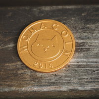 木目背景に置かれた金色のモナコインの写真