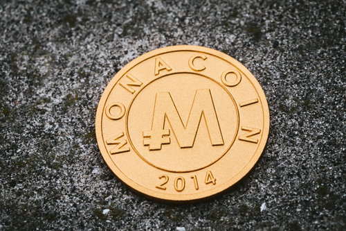 黒い背景に置かれた金色のモナコイン