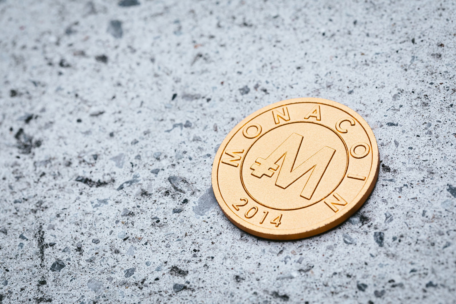灰色のコンクリート地面に置かれた金色のモナコイン
