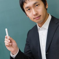 チョークを手に持って黒板の前に立つスーツ姿の先生の写真