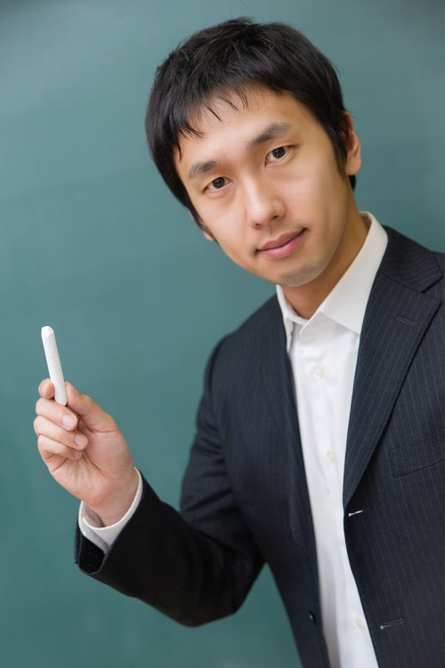 チョークを手に持って黒板の前に立つスーツ姿の先生