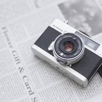 英文の新聞の上に置かれたレトロなフィルムカメラの写真