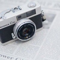 英文の新聞の上に置かれたレトロなフィルムカメラの写真