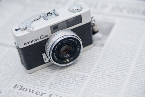 英文の新聞の上に置かれたレトロなフィルムカメラ