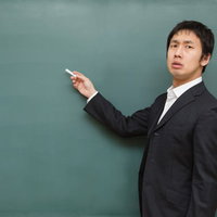 黒板の前でチョークを指先に持ち授業の準備をする講師の写真