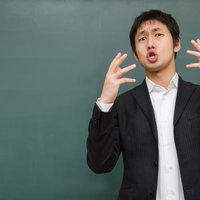 黒板の前で両手を上げて熱く訴えかける講師のポーズの写真