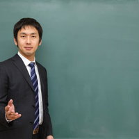 優しい表情で黒板の前に立ち授業を進める塾の講師の写真