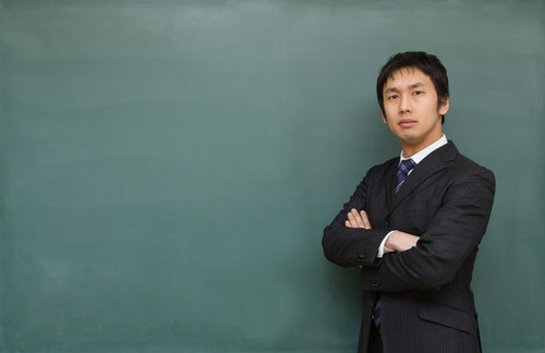 黒板の前で腕を組み気合が入った表情の教師